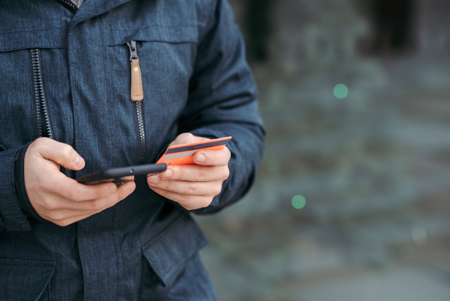 man holding credit card and browsing smartphone on street