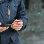 man holding credit card and browsing smartphone on street