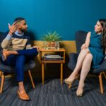 woman wearing teal dress sitting on chair talking to man