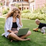 smiling blonde woman sitting with laptop in garden