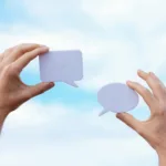 close up of man holding paper cutouts in the shape of conversational clouds