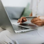 person using a macbook and holding a credit card