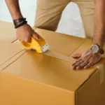crop man sealing box with scotch tape